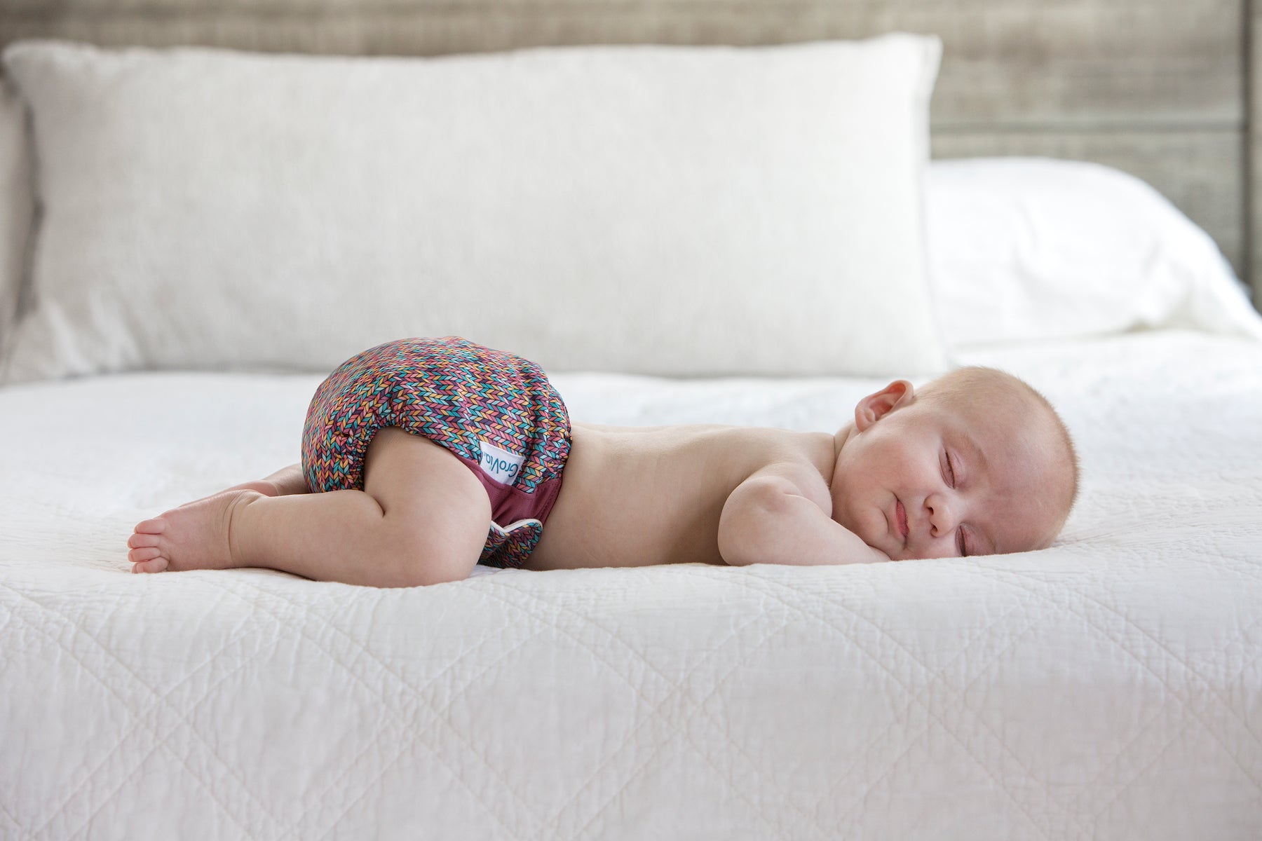 A baby wearing a Grovia reusable nappy asleep on a bed