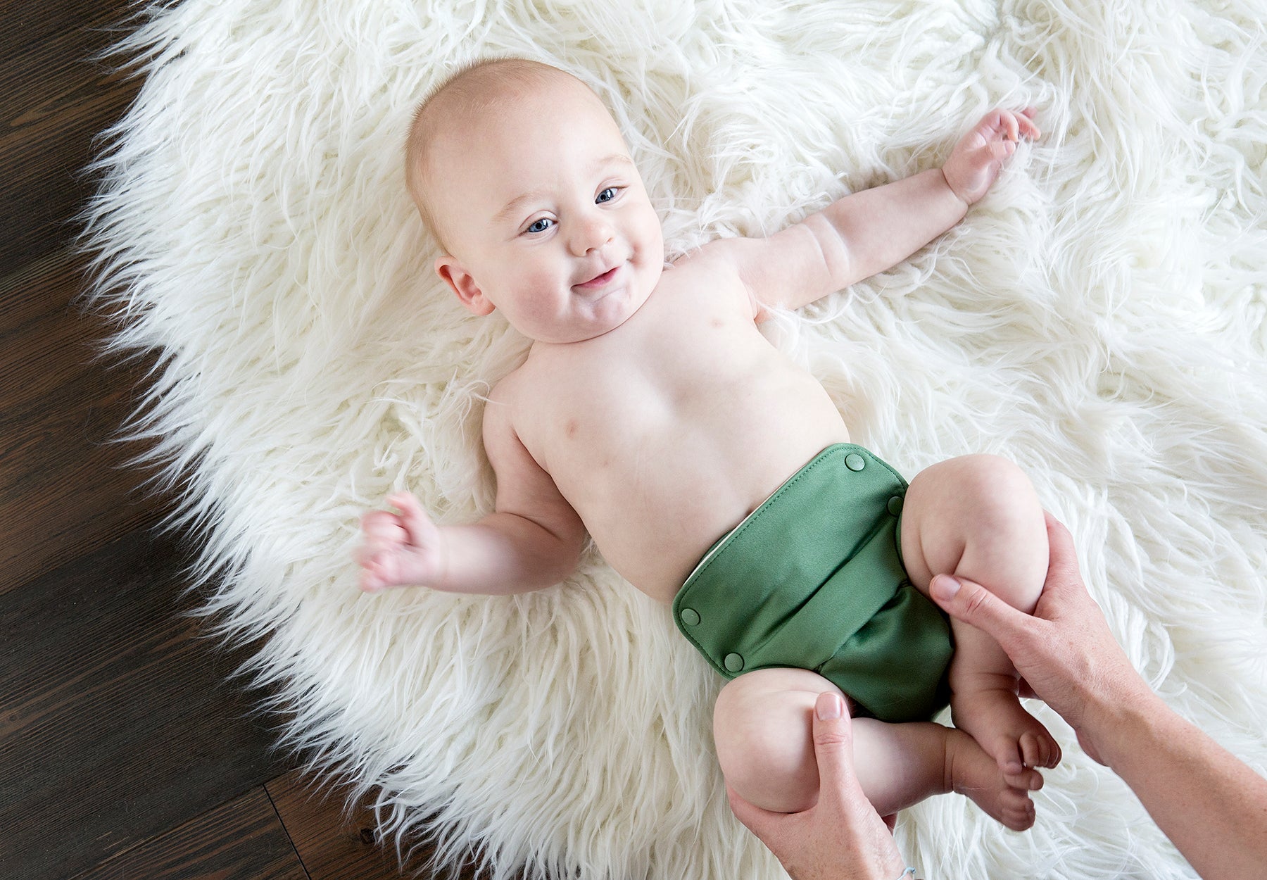 A baby wearing a green Grovia reusable nappy on a white fluffy rug