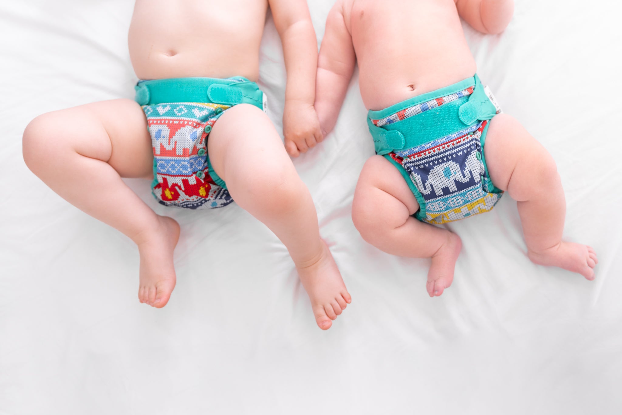 Two babies laying on a bed wearing Babipur Clyd pop=-in reusable nappies