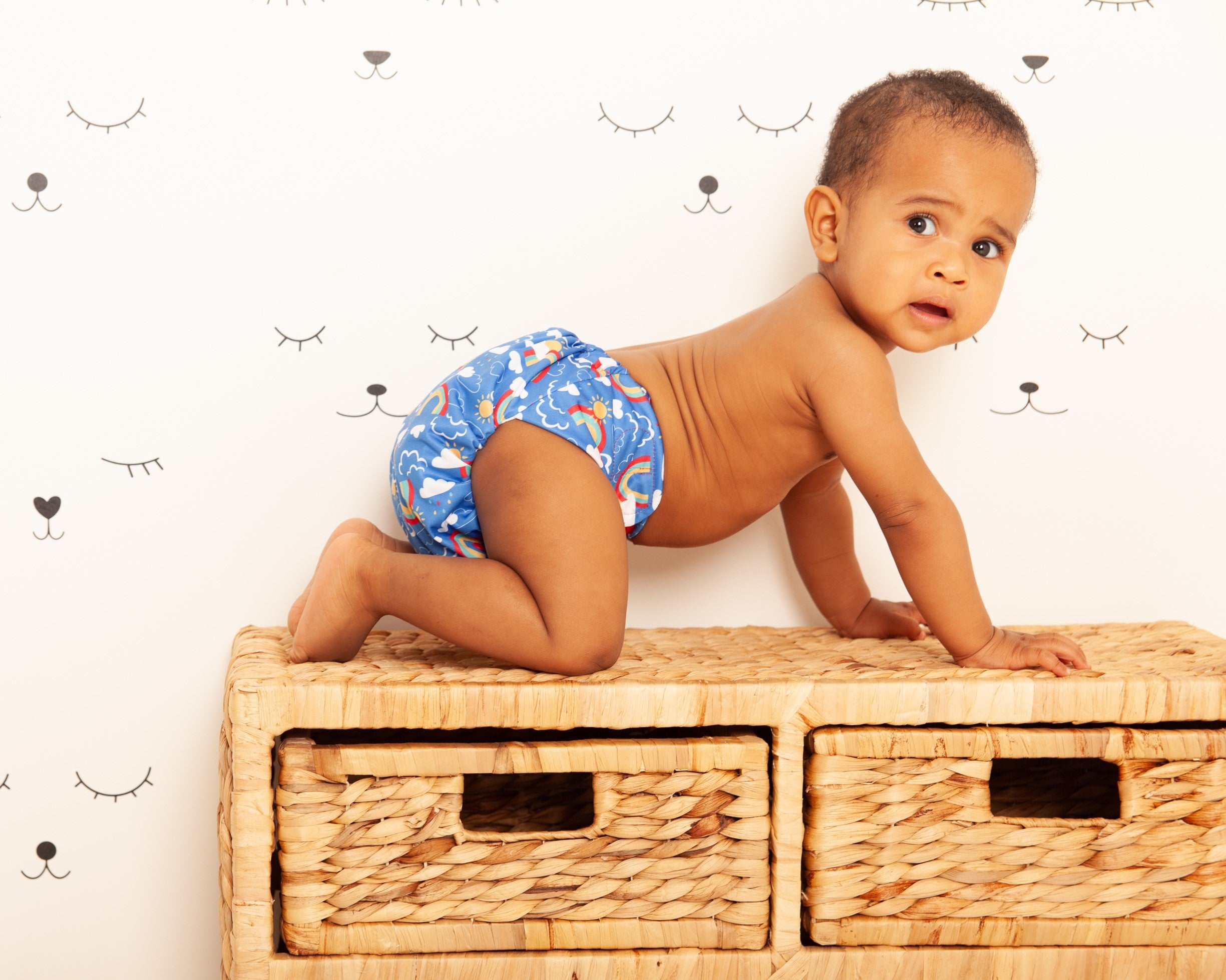 A baby wearing a Tots Bots reusable nappy on a wicker changing station