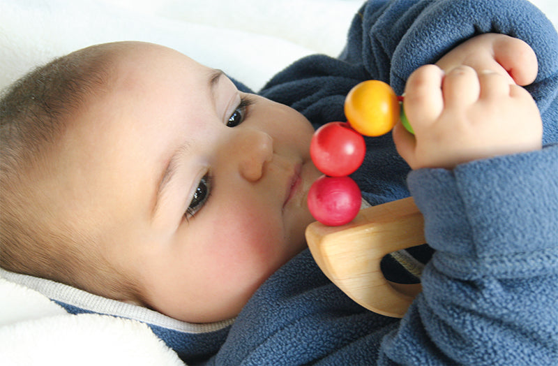 Baby holding the Grimm's Grasping Toy Rainbow Boat