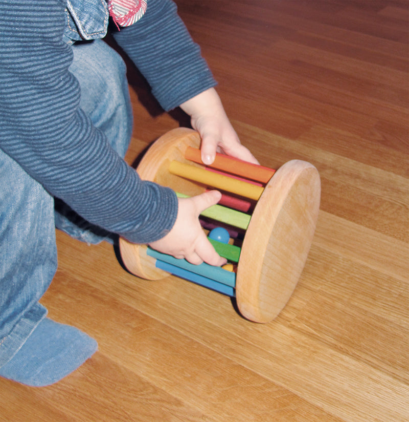 A toddler plays with the Grimm's Big Rolling Rainbow Wheel Toy on a wooden floor