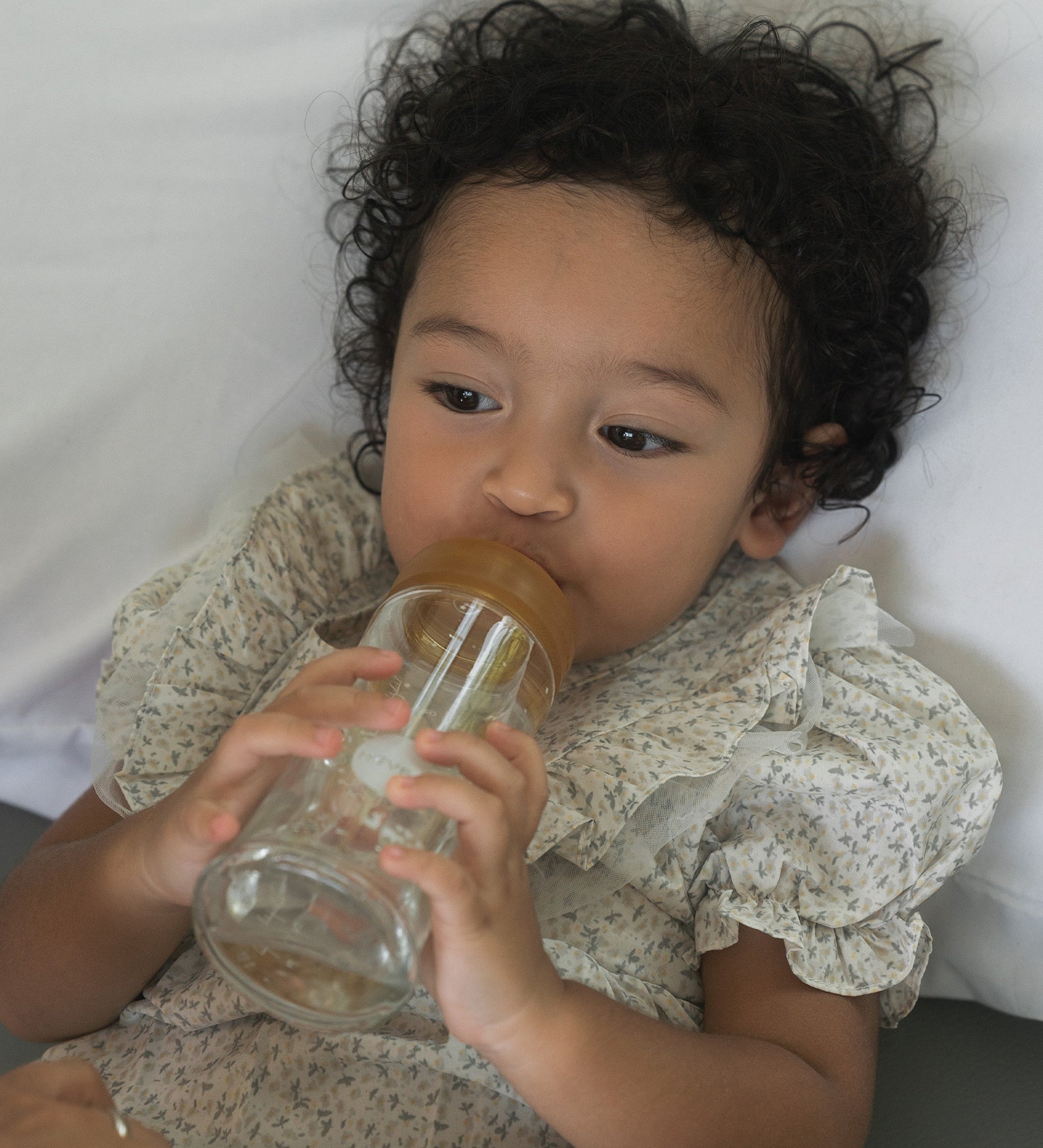 Toddler laying on a pillow with the Hevea Glass Wide Neck Bottle with natural rubber teat.