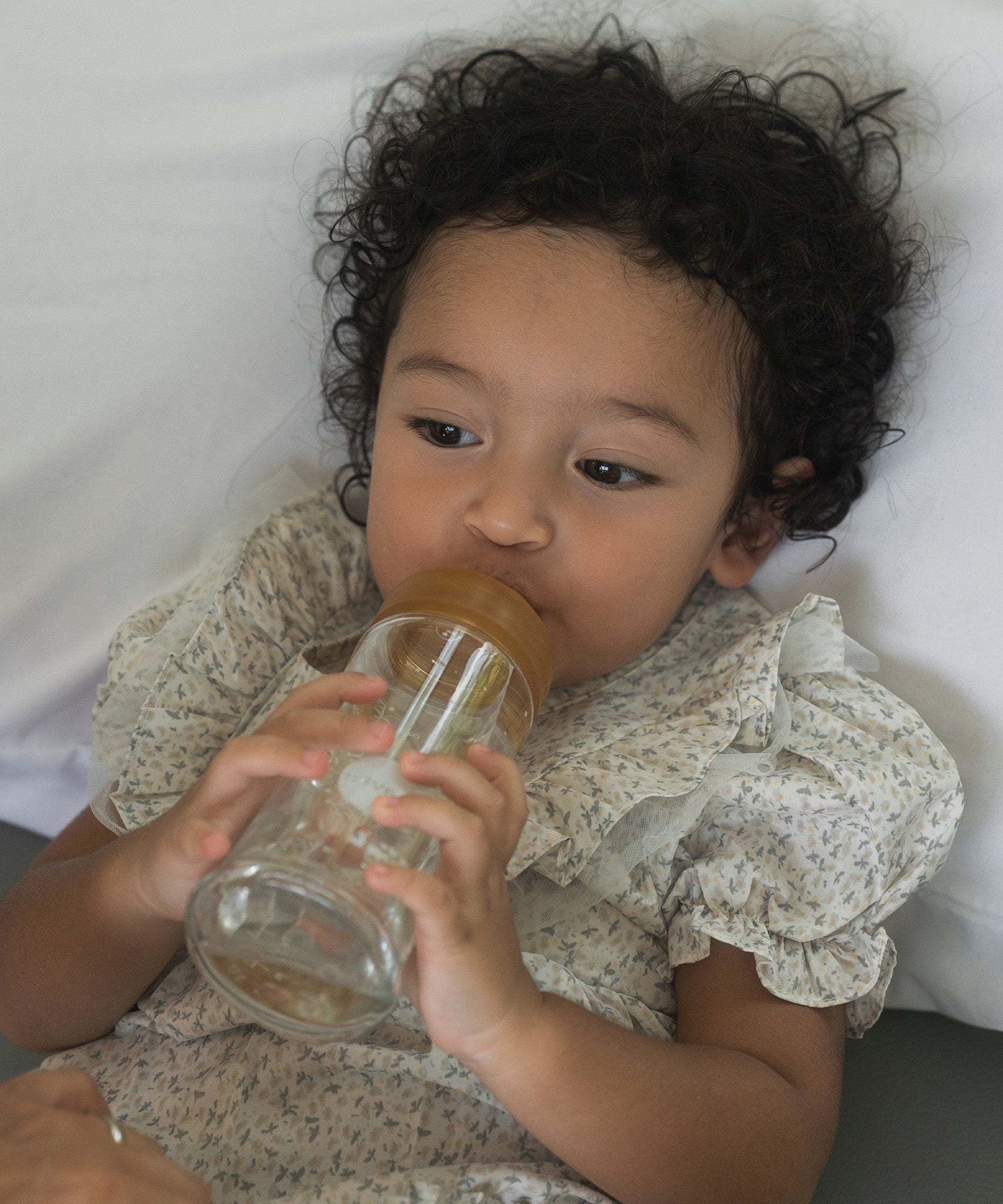 Toddler laying on a pillow with the Hevea Glass Wide Neck Bottle with natural rubber teat.