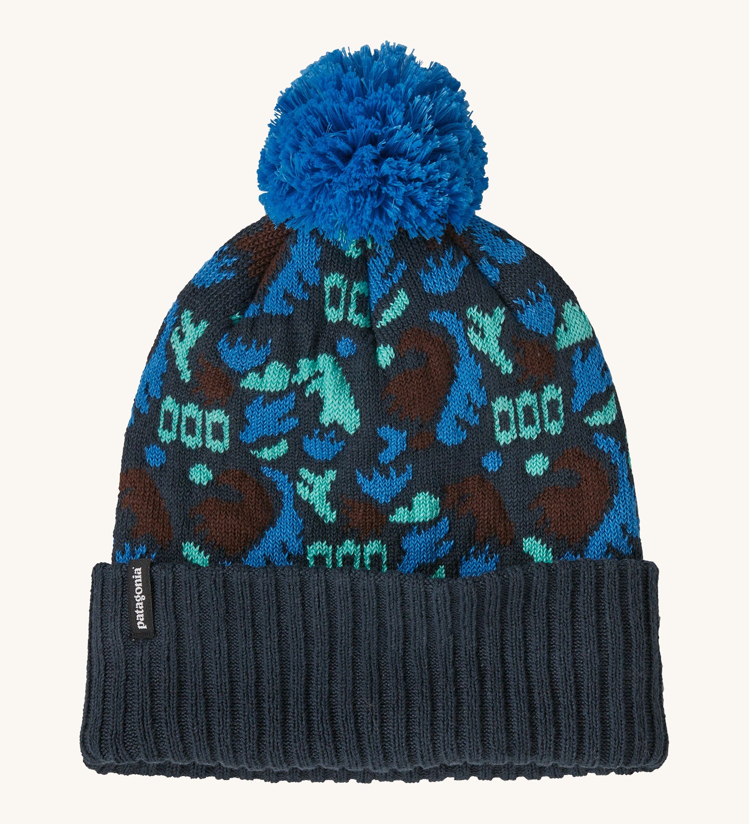 A blue Patagonia bobble beanie with different shapes and patterns on a cream background.