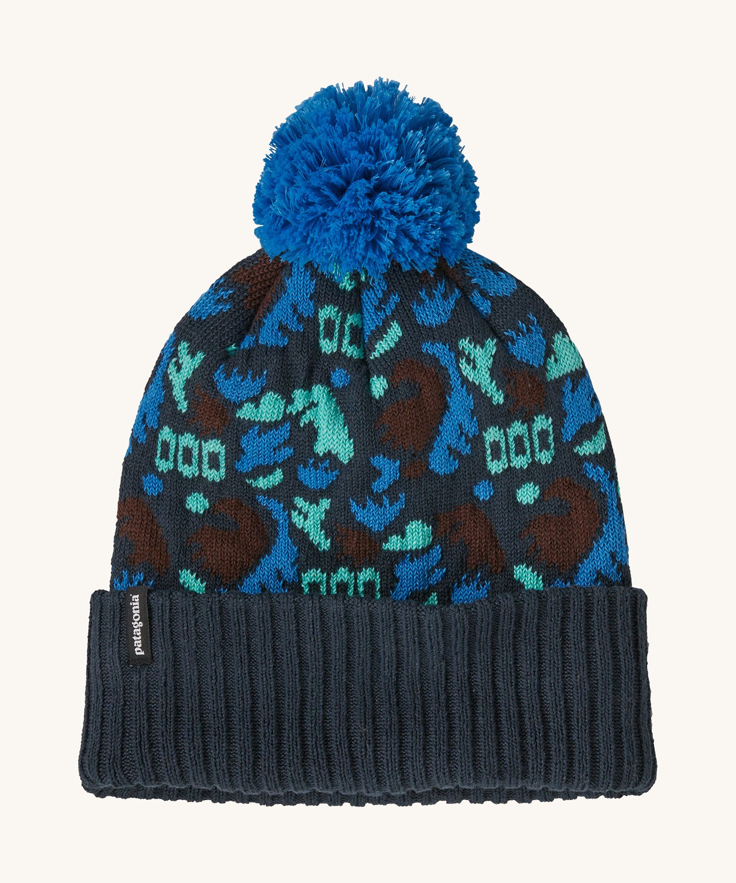 A blue Patagonia bobble beanie with different shapes and patterns on a cream background.