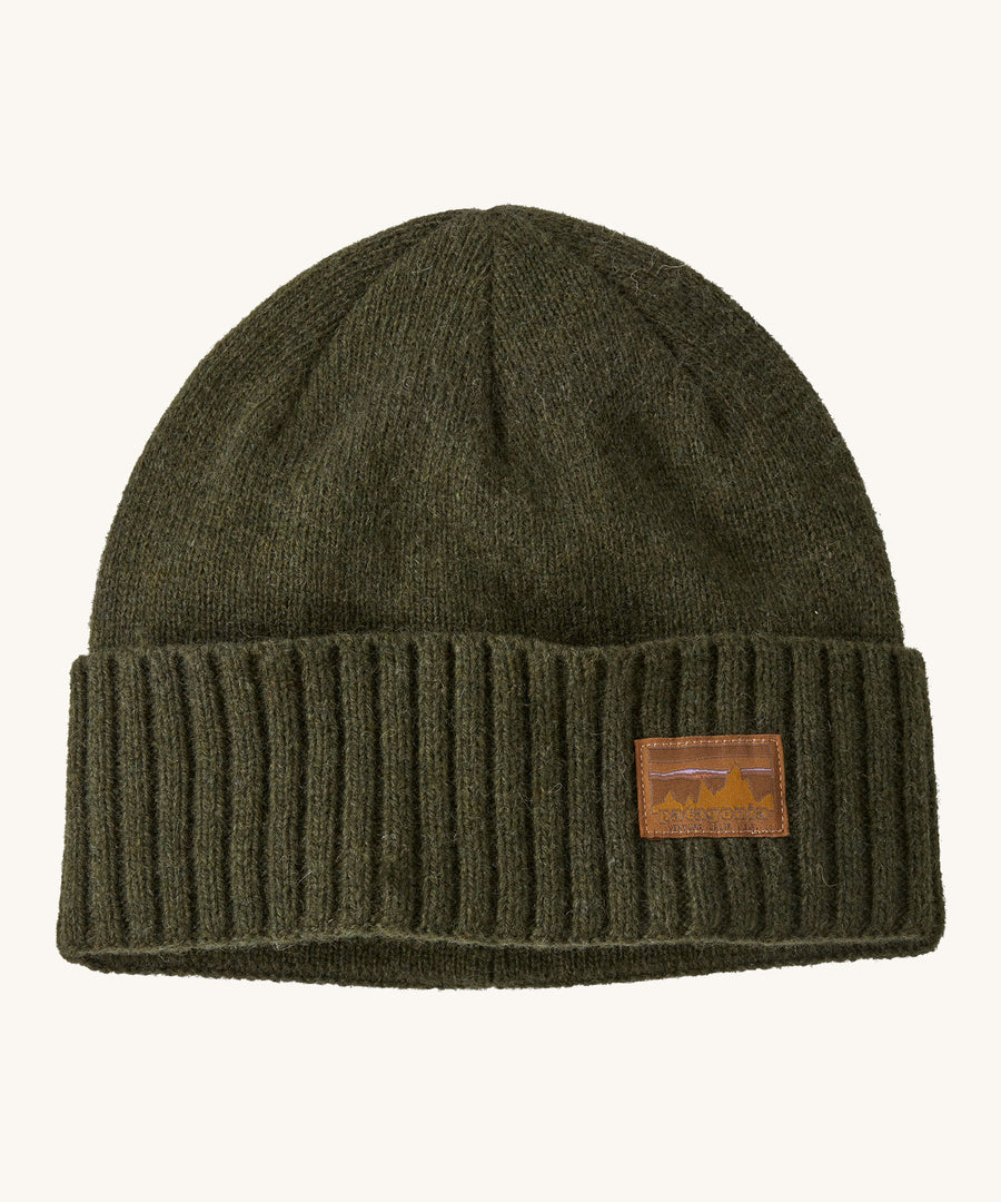 A green beanie with a Patagonia logo on the front on a cream background.