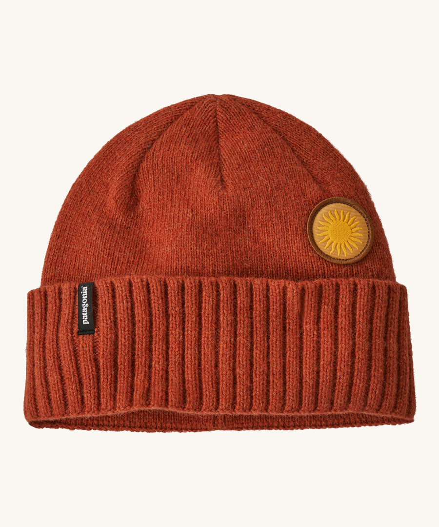 A red beanie with the Patagonia logo and sun badge on the front on a cream background.