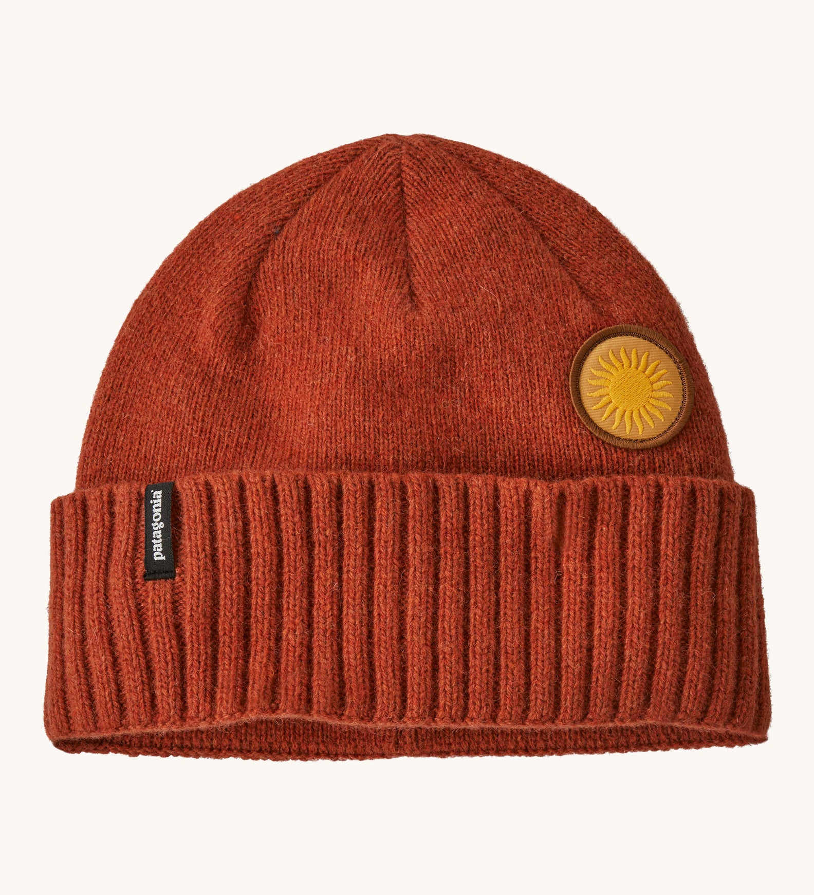 A red beanie with the Patagonia logo and sun badge on the front on a cream background.