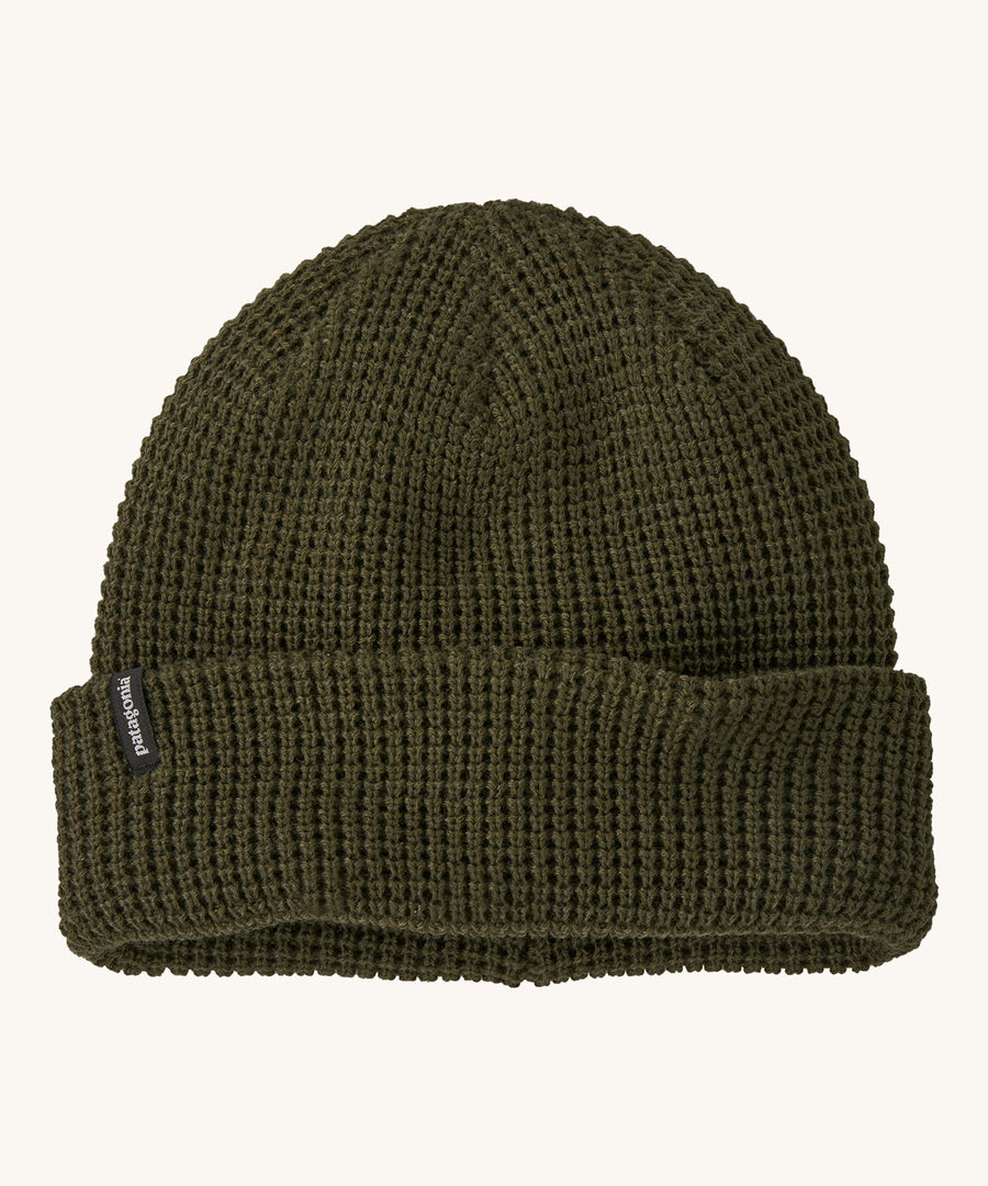 A dark green plain Patagonia beanie on a cream background.