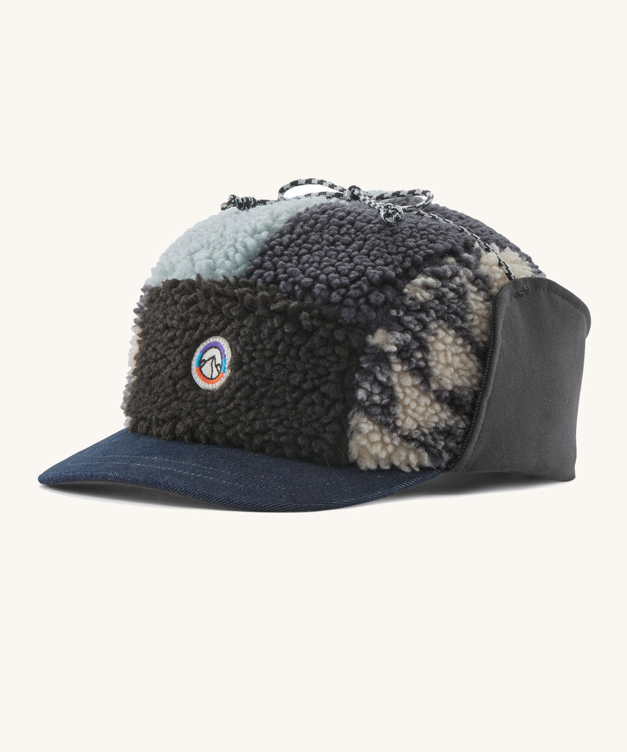 A blue fleeces earflap cap with a mountain logo on the front on a cream background