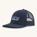 A navy Patagonia trucker hat with the Patagonia logo on the front on a cream background.