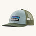  A light blue and green Patagonia trucker hat with the Patagonia logo on the front on a cream background. 