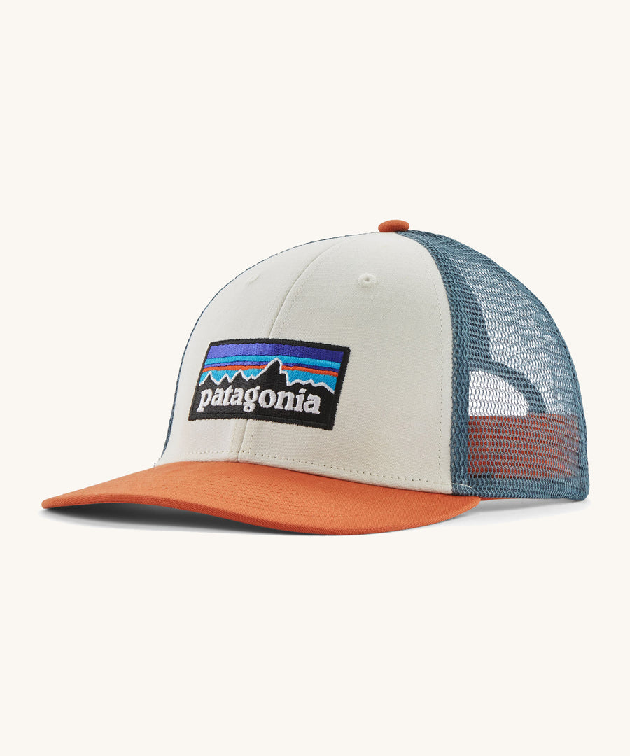 A white, blue and orange Patagonia trucker har with the Patagonia logo on the front on a cream background.