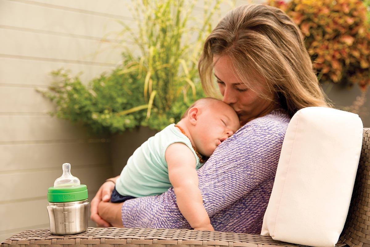 Woman sat with her baby next to the Kid Kanteen reusable metal baby bottle on a garden chair