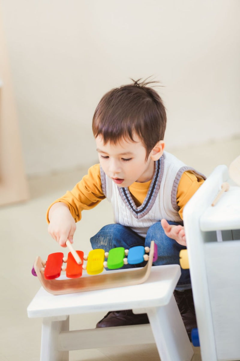 Child playing with the Plan Toys Oval Xylophone with rainbow keys and made from natural rubber wood.