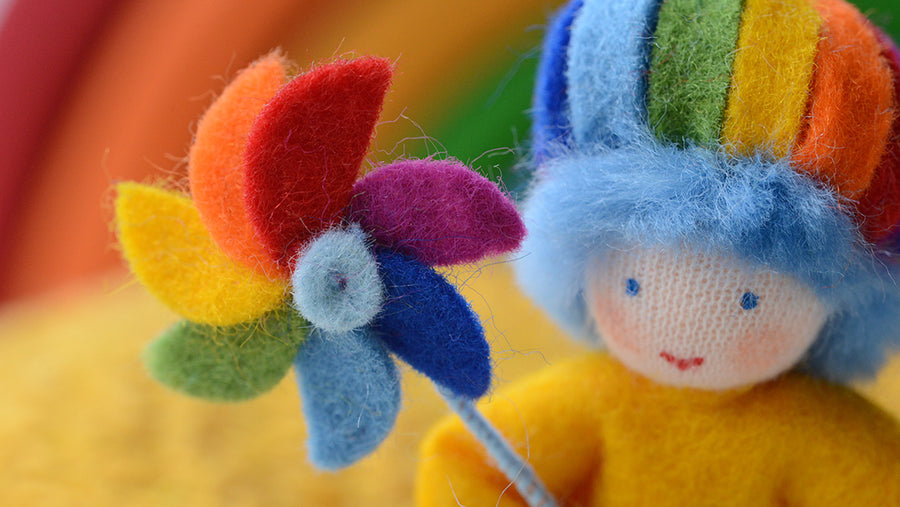 Closeup of an Ambrosius wool felted doll with a rainbow hat and windmill