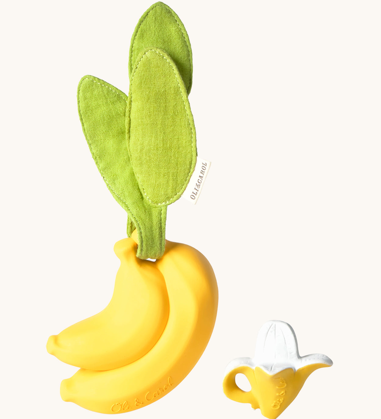 The Ana Banana Pacifier Holder on a cream background. The image shows an Oli & Carol banana teething toy next to the holder. The banana is smooth and has a green muslin leaf attachment on the top to tie the holder to a pram handle, high chair etc.