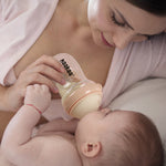 A parent feeding their child with the Haakaa Generation 3 Glass Baby Bottle in peach