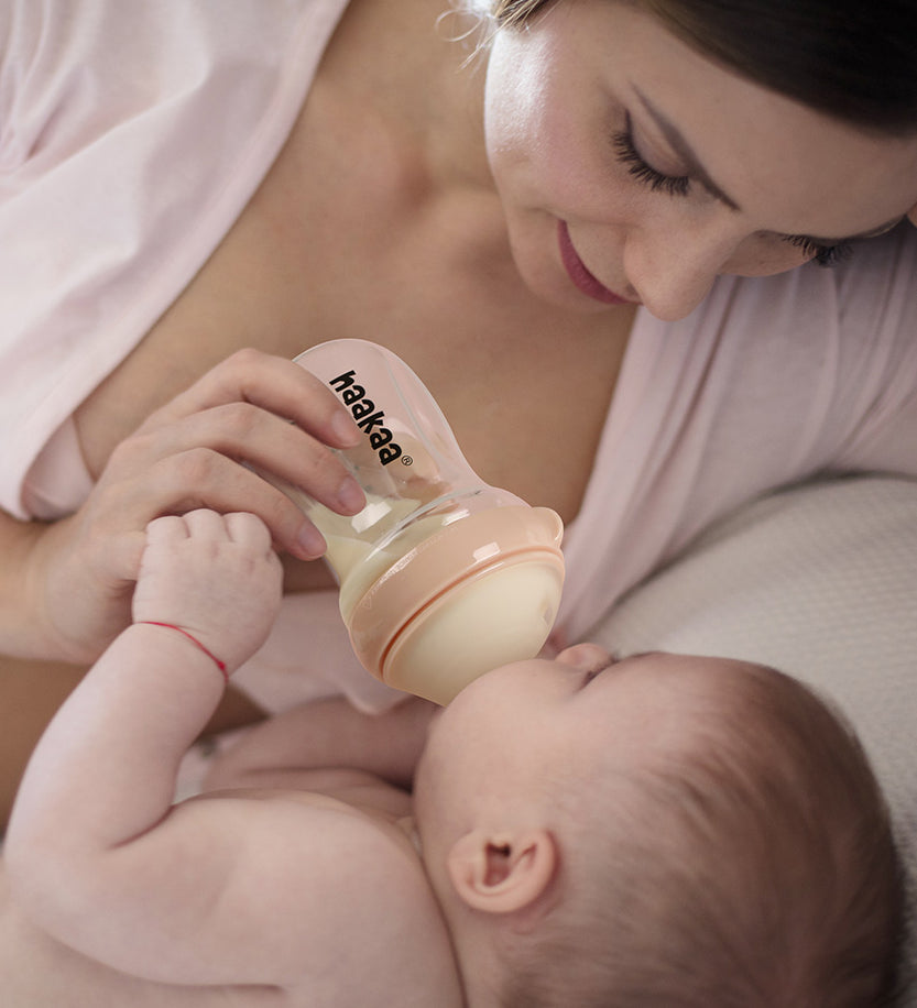 A parent feeding their child with the Haakaa Generation 3 Glass Baby Bottle in peach