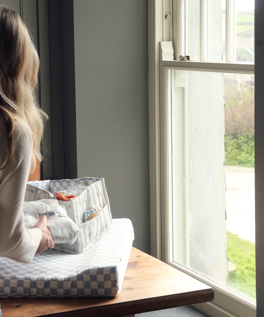 A person by a window, placing the Coastline Nappy Caddy on top of the Waves Changing Mat