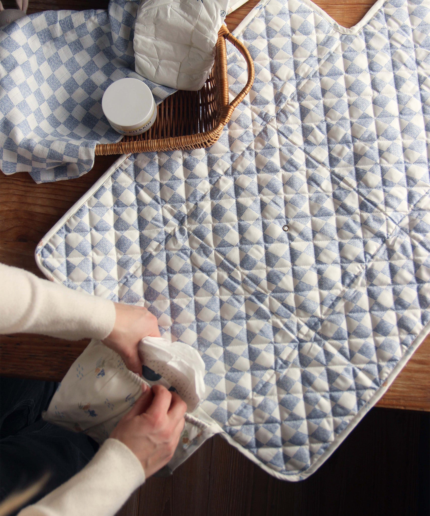 Avery Row Travel Changing Mat - Coastline in adults hands, unfolded on a wooden table, showing the pocket at the end of the mat.