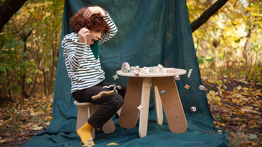 Child sat on a Babi wooden stool and playing with toys