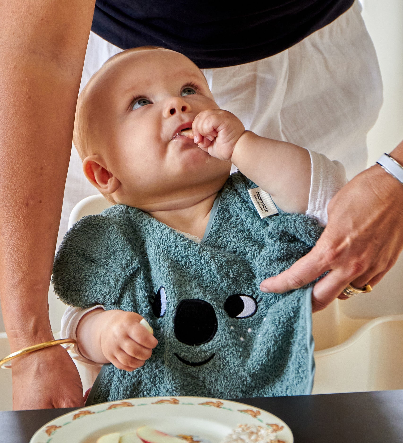 A child eating food at a table whilst wearing the Roommate Organic Cotton Baby Bib - Koala