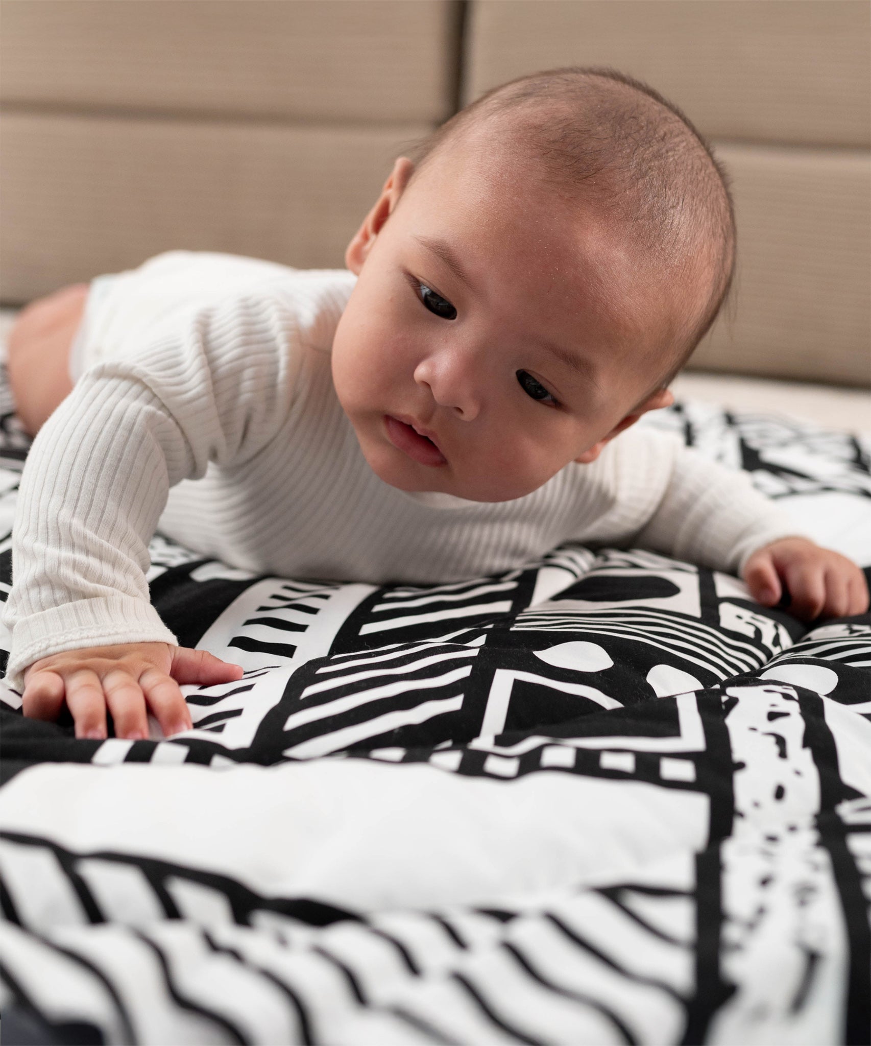 A baby looking at the monochromatic, black and white shapes on the Etta Loves x Camille Walala Reversible Playmat