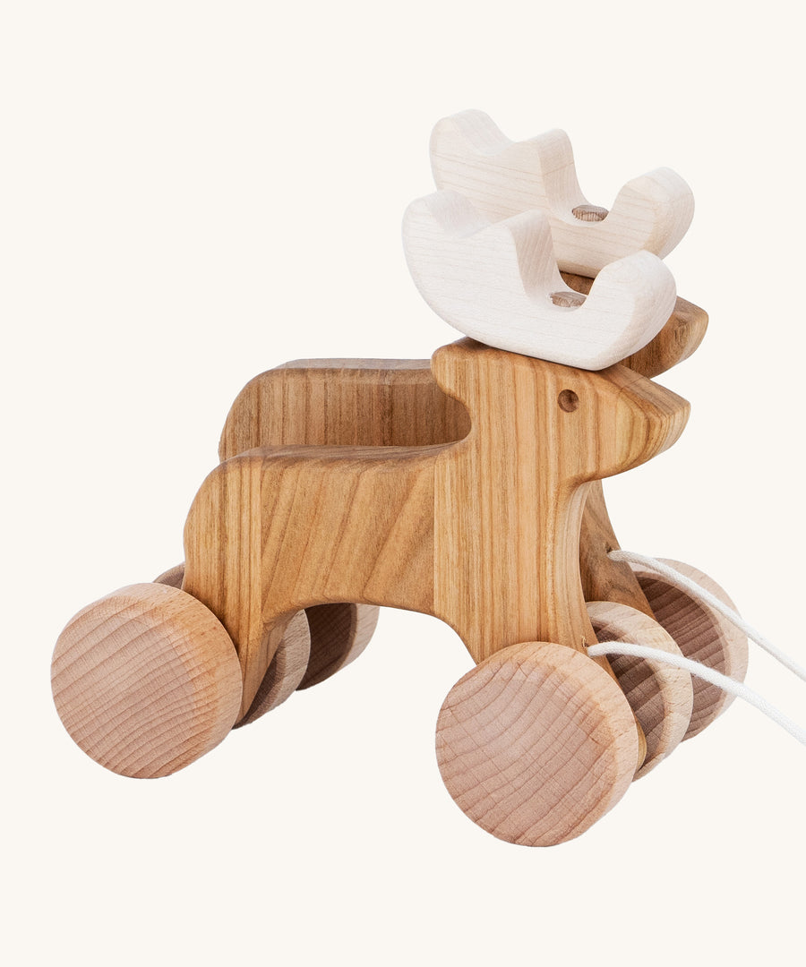 A side on view of the Bajo Pull Along Jumping Reindeer, showing the natural wood and white antlers of the reindeer. The image also shows how the two reindeer's are attached together by two wooden wheels. The image is on a cream background