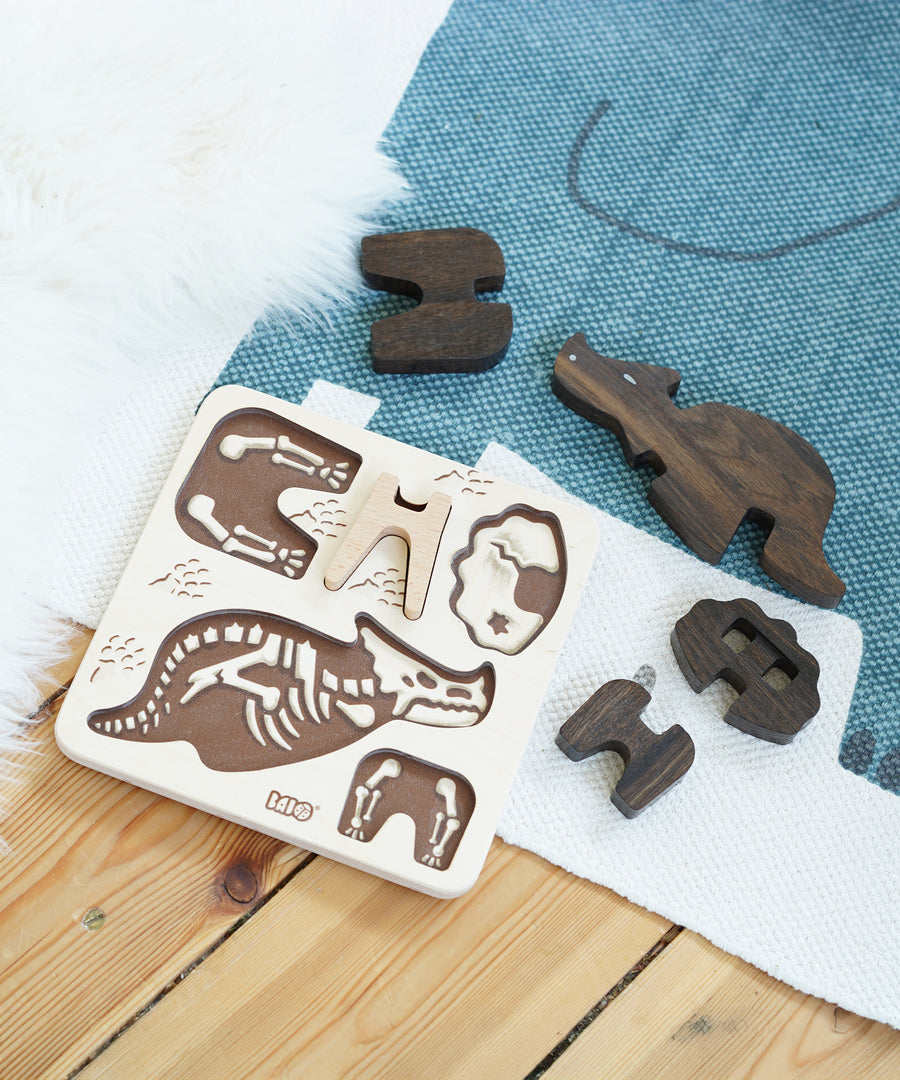 The Bajo Puzzle & Sorter - Black Oak Triceratops and puzzle board laid out on a blue and white rug on a wooden floor