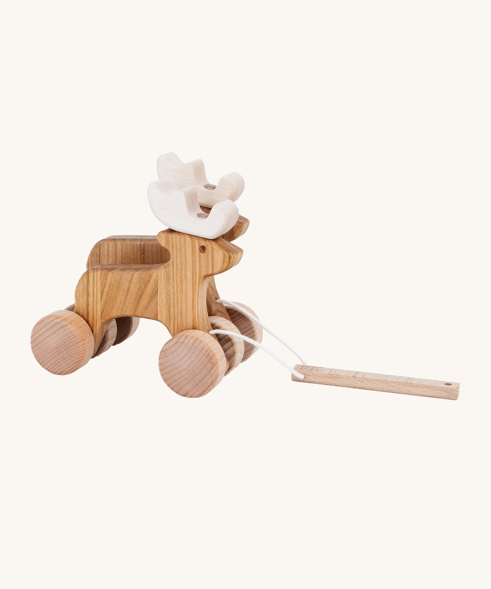 A side on view of the Bajo Pull Along Jumping Reindeer, showing the natural wood and white antlers of the reindeer. The image also shows how the two reindeer's are attached together by two wooden wheels. The mage is on a cream background