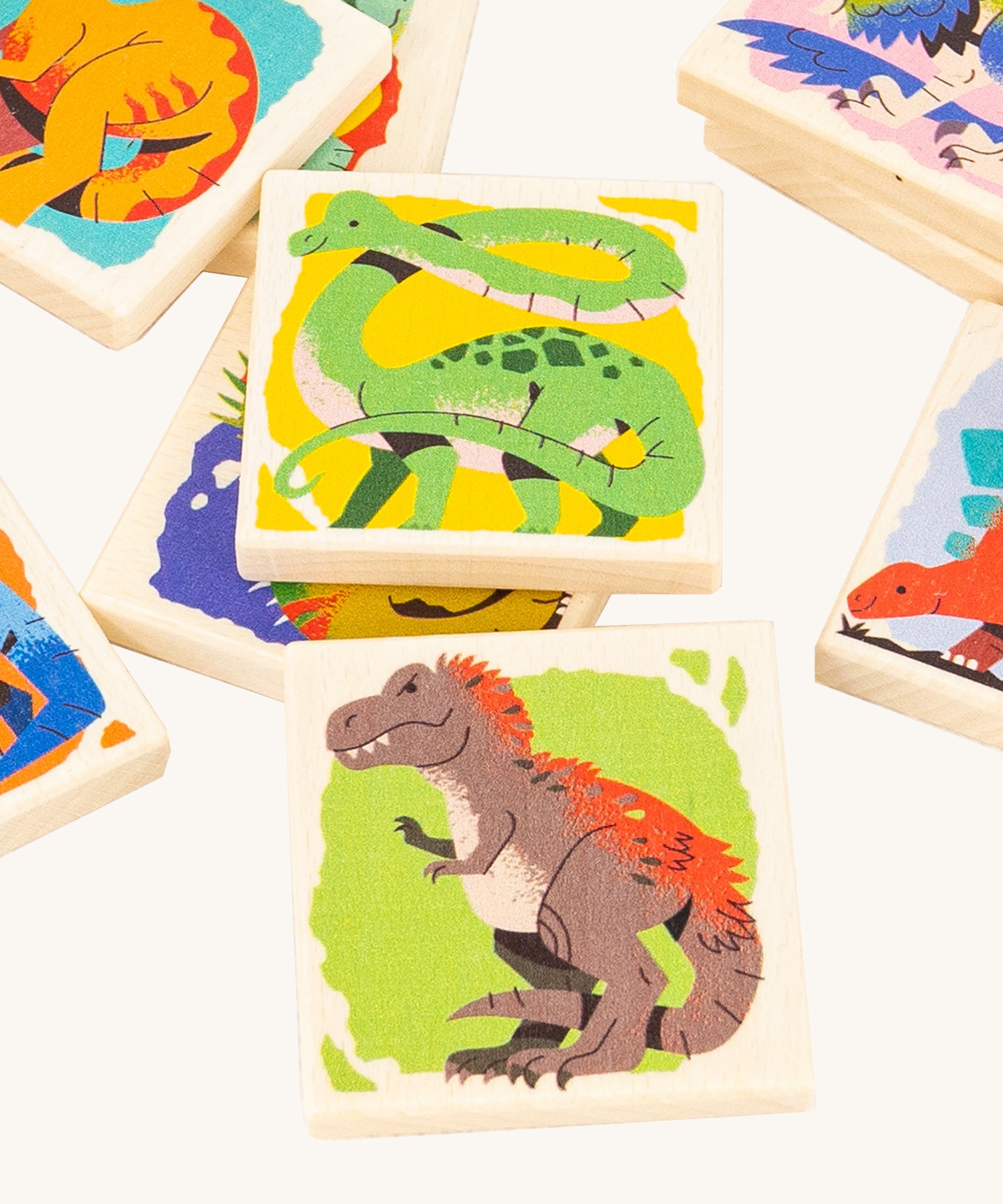 A closer look at the square dinosaur memory game pieces from the Bajo Dinosaur Memory Game, showing images of dinosaurs, on a cream background