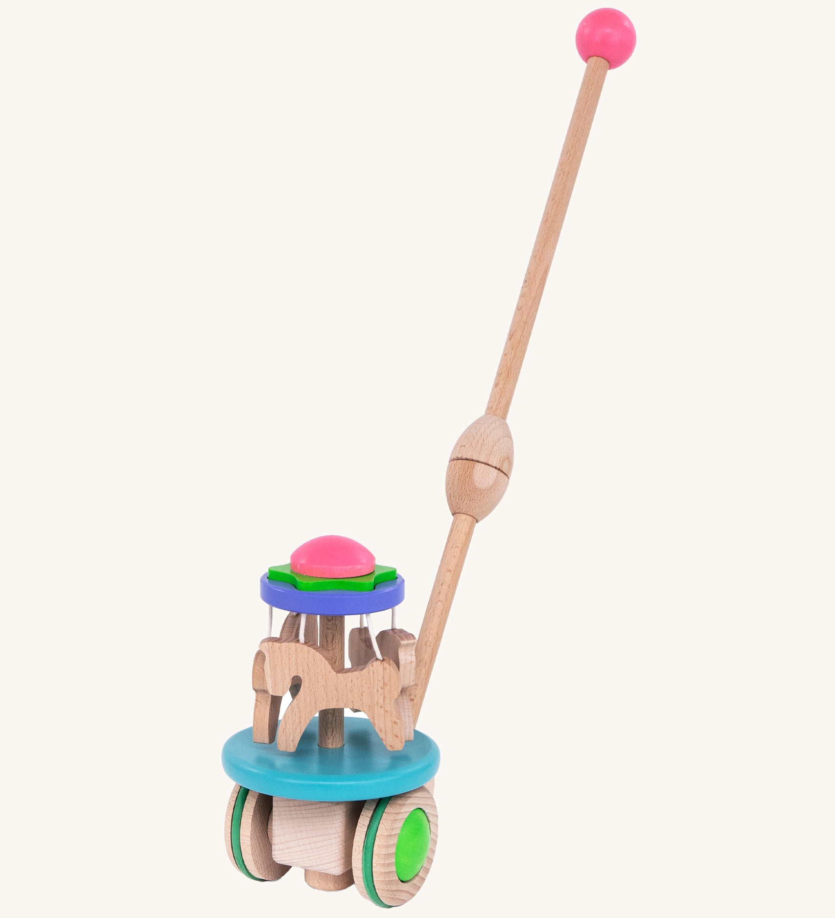 The Bajo Push Along Carousel has a long wooden handle with a pink wooden ball on top. It also has wooden horses which spin around when the toy is pushed along the ground. The Carousel is blue, purple, green, pink and natural wood in colour. The image is on a cream background