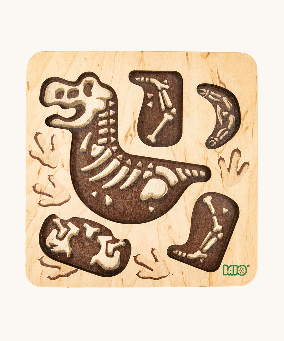 The puzzle board from the Bajo Puzzle & Sorter - Black Oak T-Rex, showing dinosaur bones. On a cream background