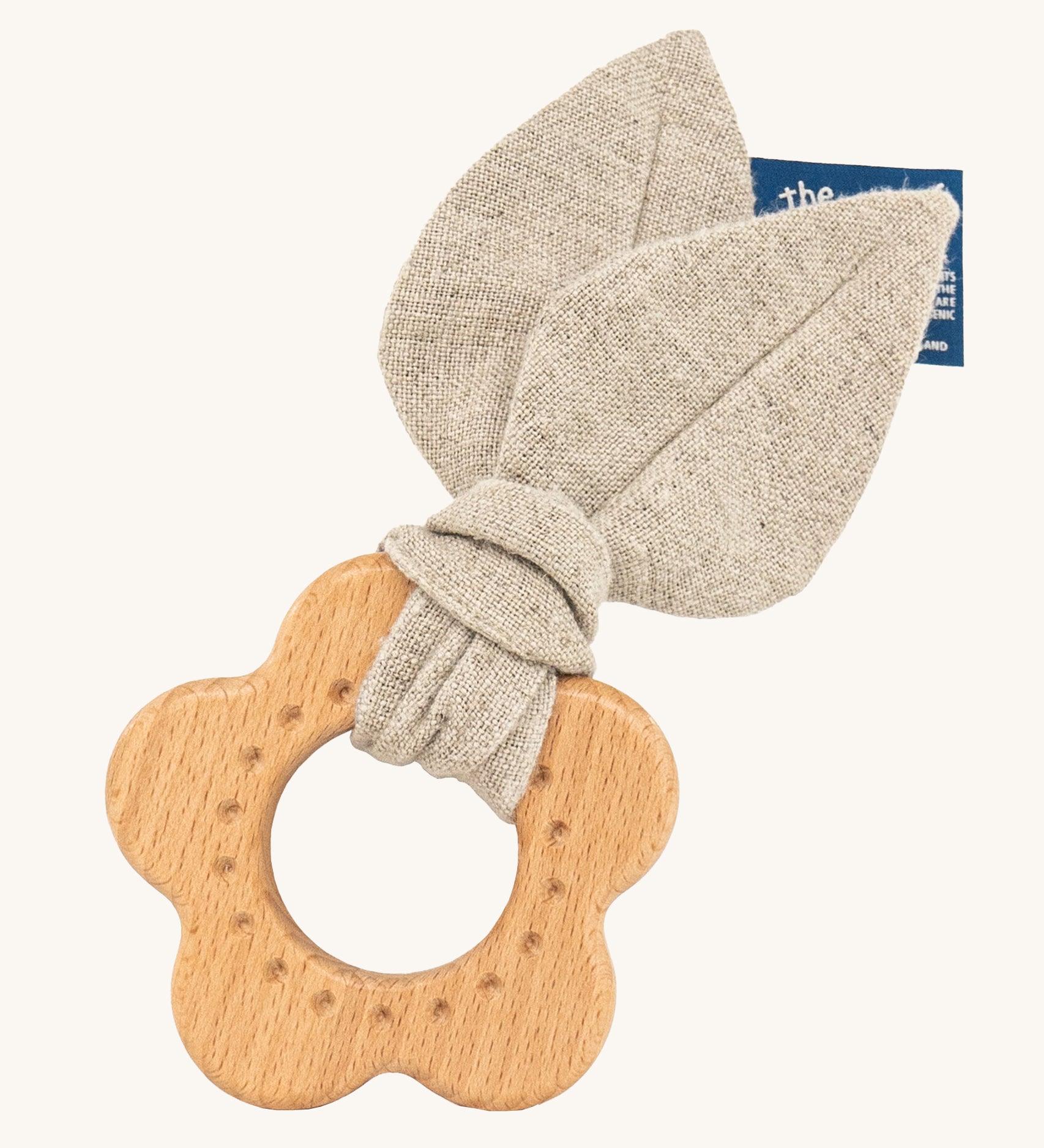 The Hempions Flower Baby Teether is an adorable baby teething toy made from natural hemp textile and solid wood, in the shape of a flower. The image shows the wooden flower teething ring with a light grey/beige hemp leaf fabric attached to it, on a cream background