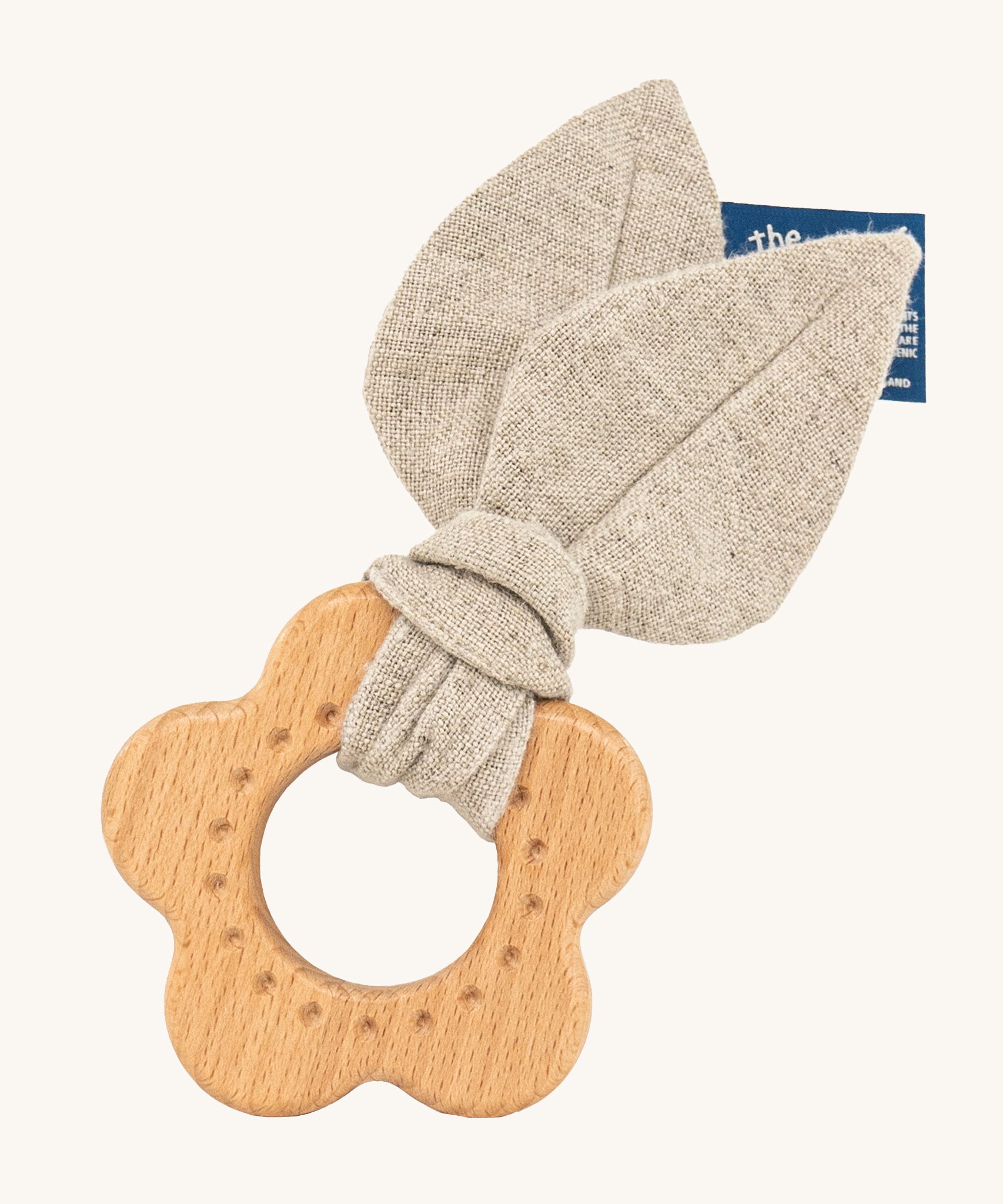 The Hempions Flower Baby Teether is an adorable baby teething toy made from natural hemp textile and solid wood, in the shape of a flower. The image shows the wooden flower teething ring with a light grey/beige hemp leaf fabric attached to it, on a cream background