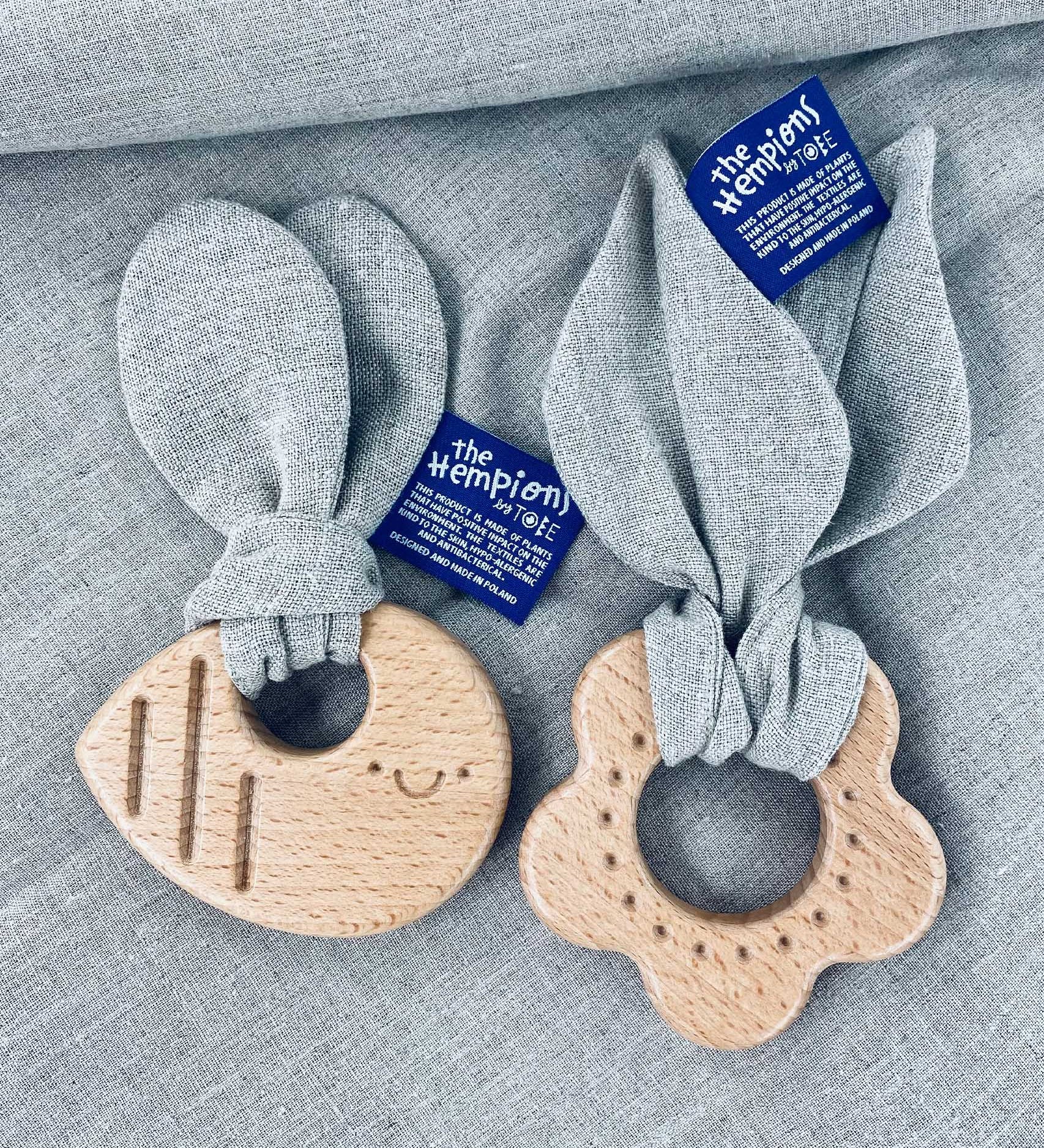 The Hemptons Flower and Bee baby teething rings, next to each other on a grey hemp fabric