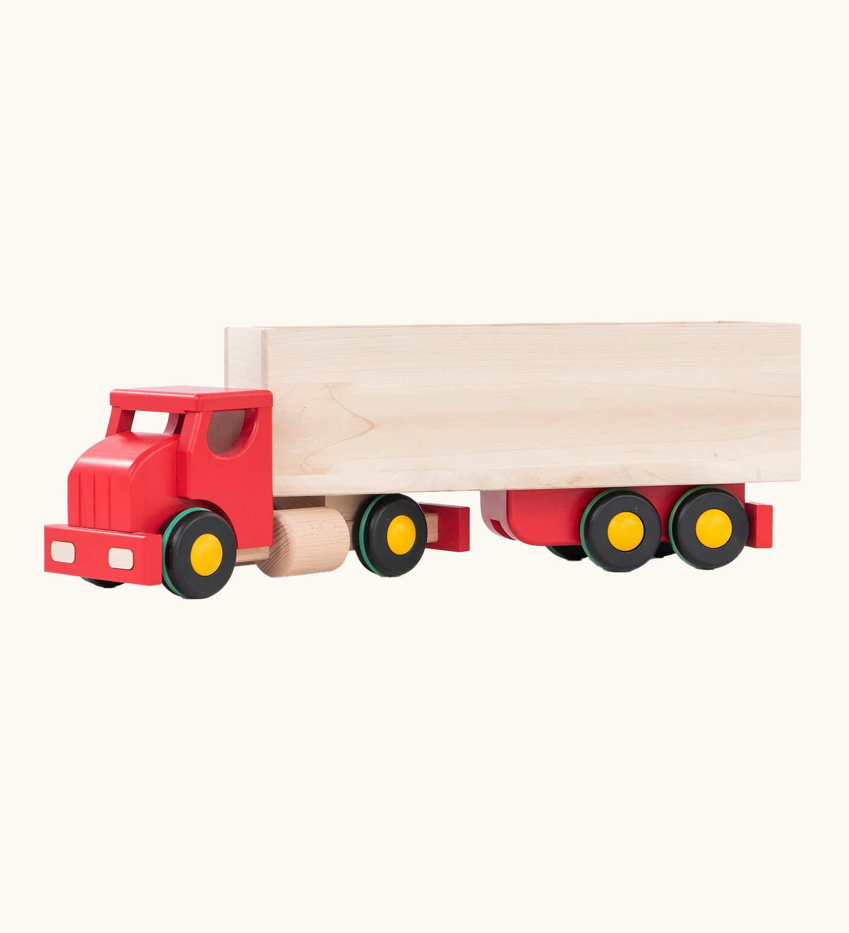 The Bajo Large Truck & Trailer has a natural wood box container on the back of a red truck cab, with black wheels with yellow hubs and a green stripe around the tire. The image has been taken from the side and is on a cream background