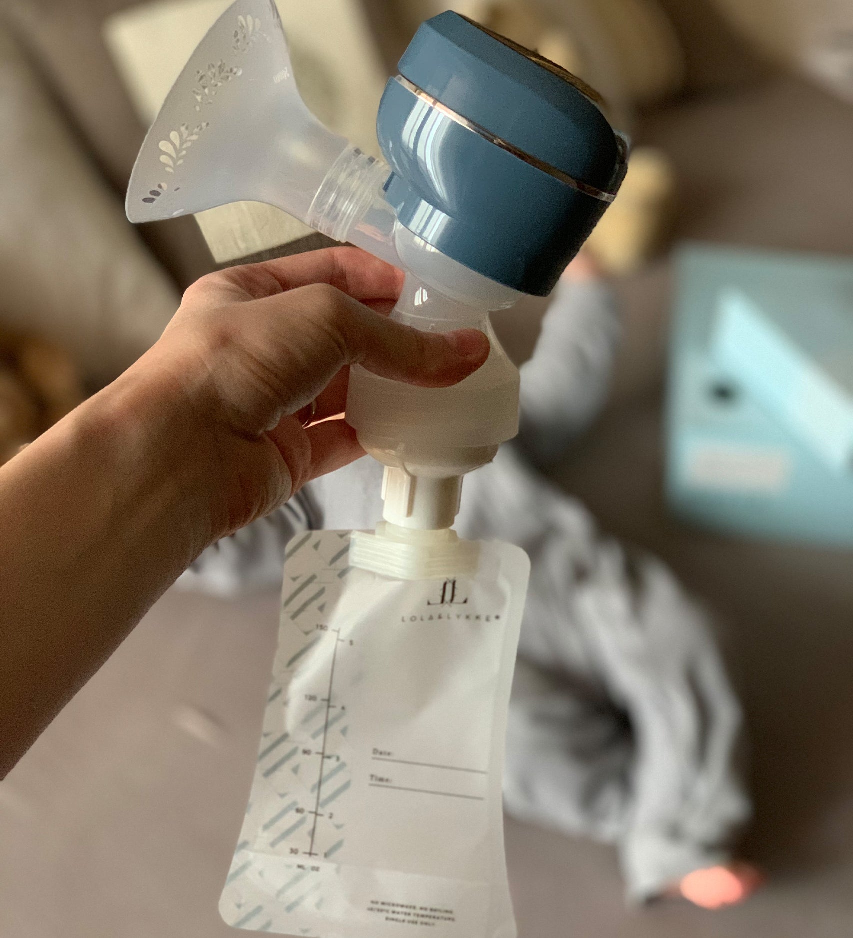 A person holding the top of the Lola&Lykke Smart Electric Breast Pump, with a milk bag attached to show how the bag attaches to the pump. This is perfect for storing breast milk for later