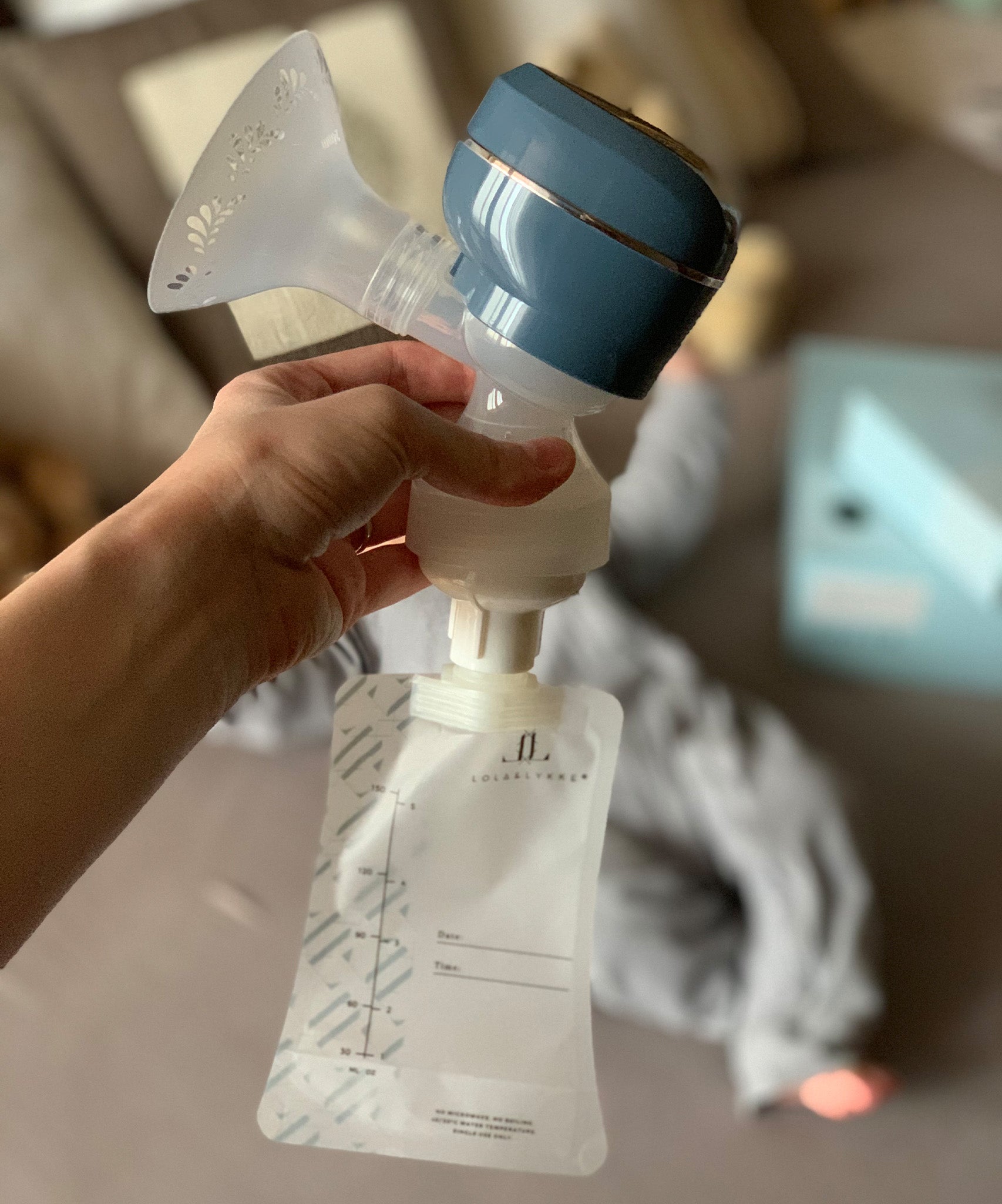 A person holding the top of the Lola&Lykke Smart Electric Breast Pump, with a milk bag attached to show how the bag attaches to the pump. This is perfect for storing breast milk for later