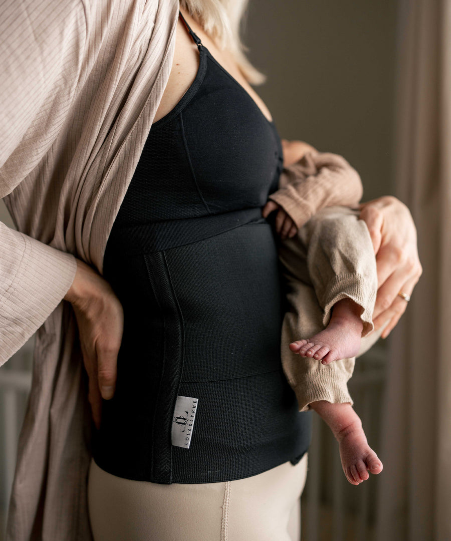 A person holding a baby in their arms, wearing the Lola & Lykke Core Restore Postpartum Belly Band