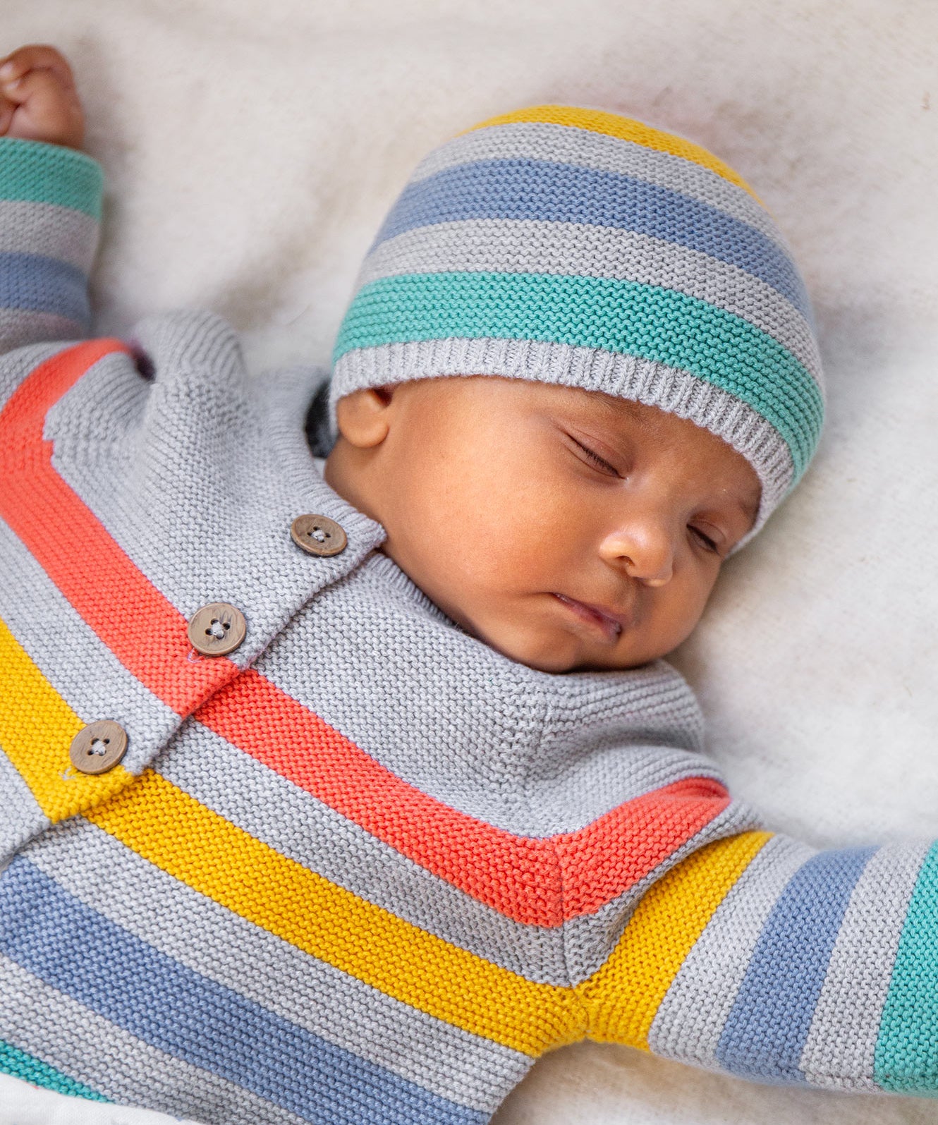 A child wearing the Frugi Bright As A Button Cardi - Grey Marl Stripe, and the same pattern Frugi Hat