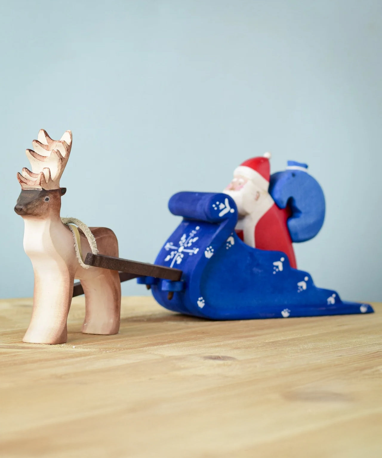 Bumbu Santa sitting in the back of the Snow Sleigh with a blue wooden sack on his back, and a Reindeer attached to the reins of the sleigh