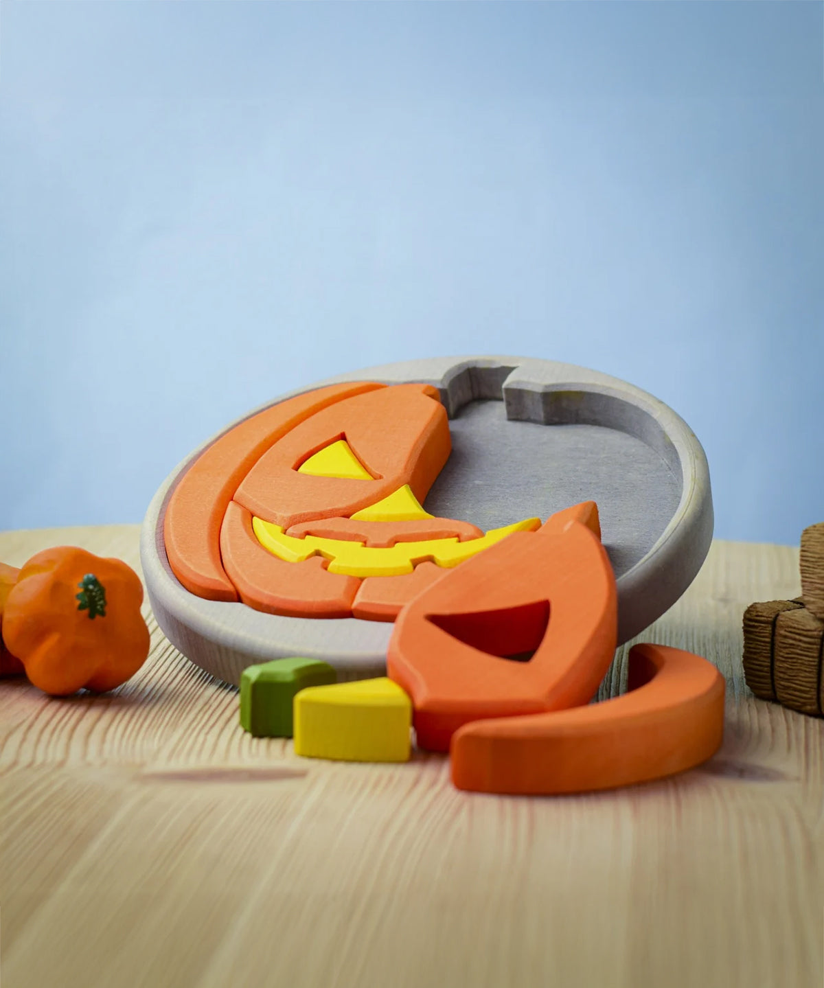 The Bumbu Toys Halloween Pumpkin Puzzle with a grey puzzle board, is an orange and yellow pumpkin puzzle, with removable pumpkin sections. Perfect for Halloween games. This image shows part of the pumpkin puzzle in the wooden board, and some pieces in front of the puzzle.