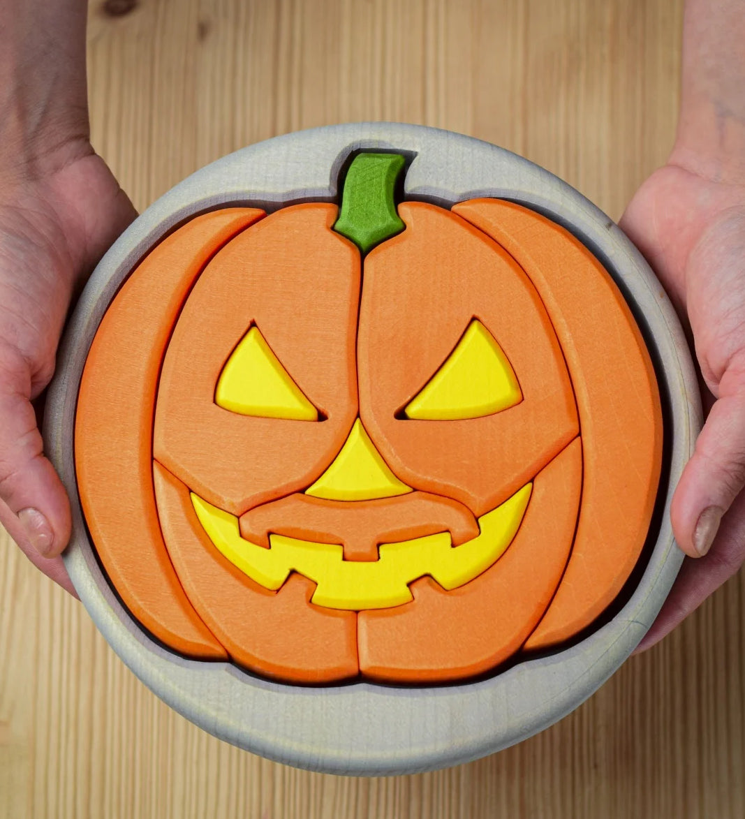 A person holding the Bumbu Toys Halloween Pumpkin Puzzle - Grey, in their hands. The image is a close up view of the pumpkin puzzle from above, showing the different puzzle sections