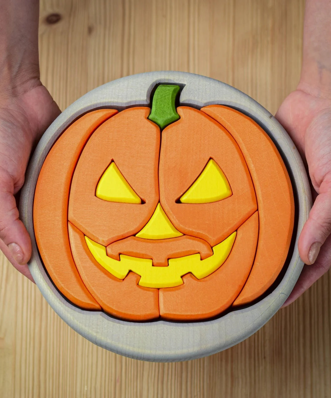 A person holding the Bumbu Toys Halloween Pumpkin Puzzle - Grey, in their hands. The image is a close up view of the pumpkin puzzle from above, showing the different puzzle sections