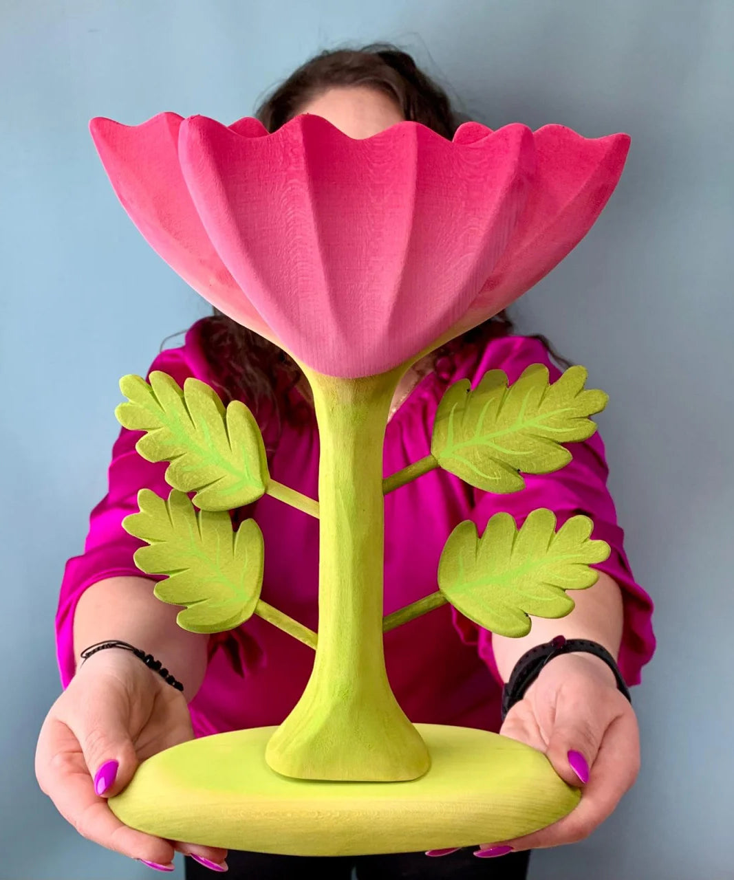 A person holding up the Bumbu Wooden Large Pink Flower in front of them.