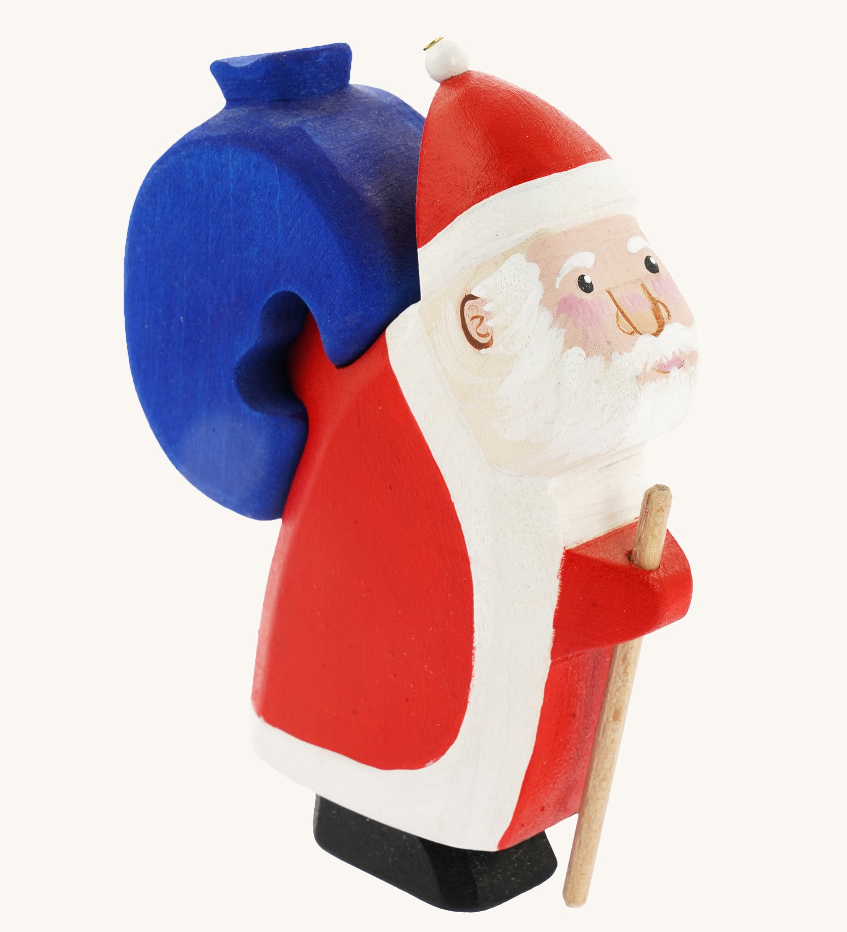 Bumbu Wooden Santa Claus, is a handmade and hand painted festive toy figure with a wooden blue sack that can be removed from its back. The image shows Santa with rosy cheeks, a beard, a red and white outfit and a red and white hat, with the blue wooden sack on his back. The image is on a cream background