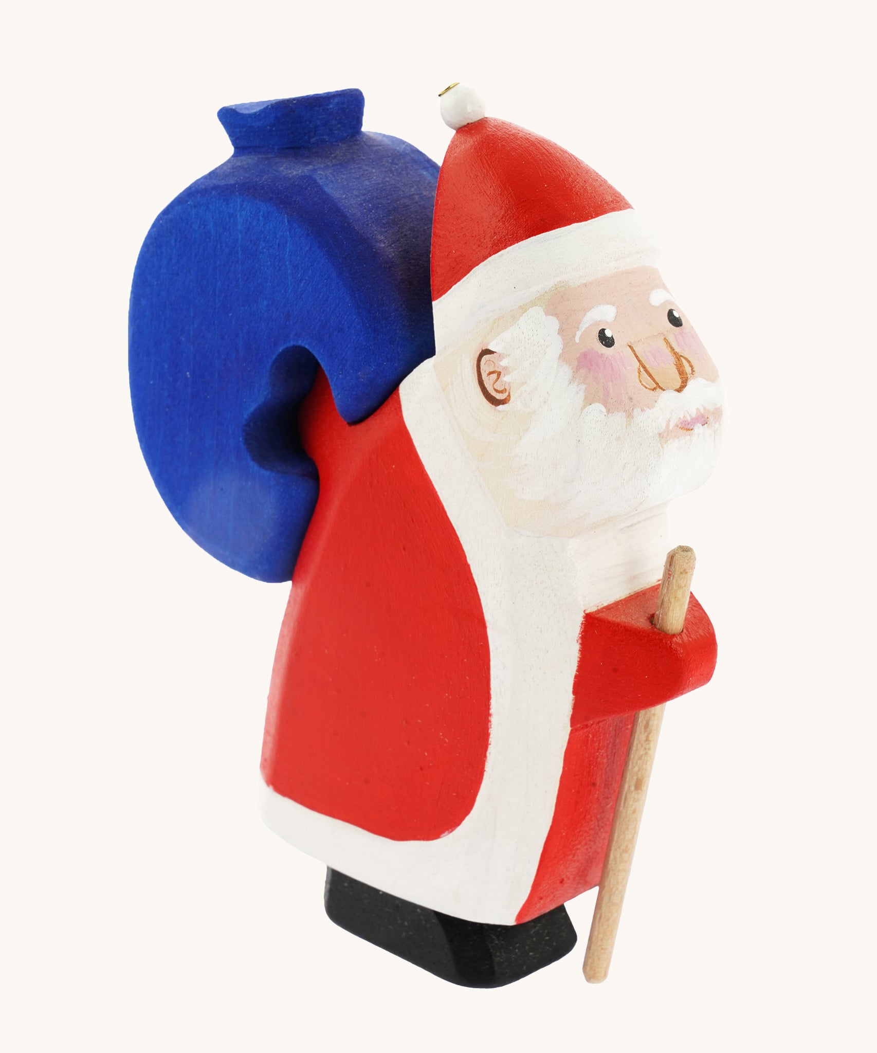 Bumbu Wooden Santa Claus, is a handmade and hand painted festive toy figure with a wooden blue sack that can be removed from its back. The image shows Santa with rosy cheeks, a beard, a red and white outfit and a red and white hat, with the blue wooden sack on his back. The image is on a cream background